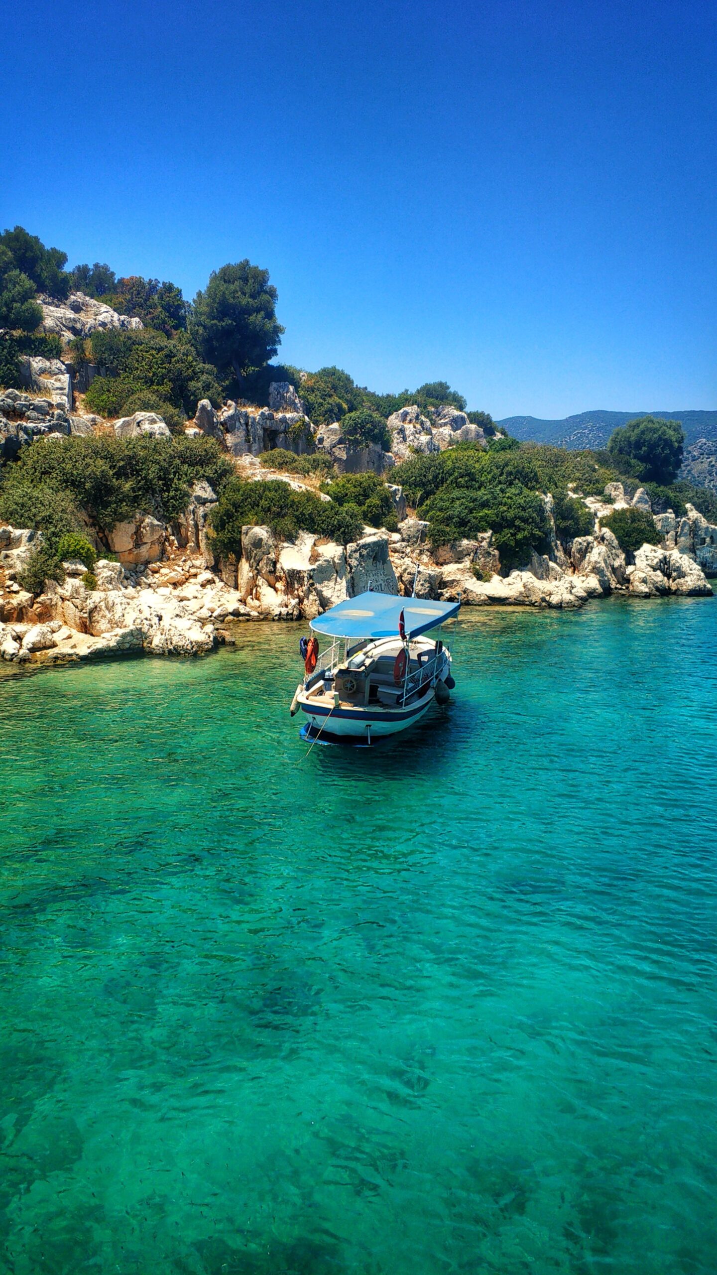 Scenic view of a boat on pristine turquoise waters in Antalya, Türkiye, under a clear blue sky.