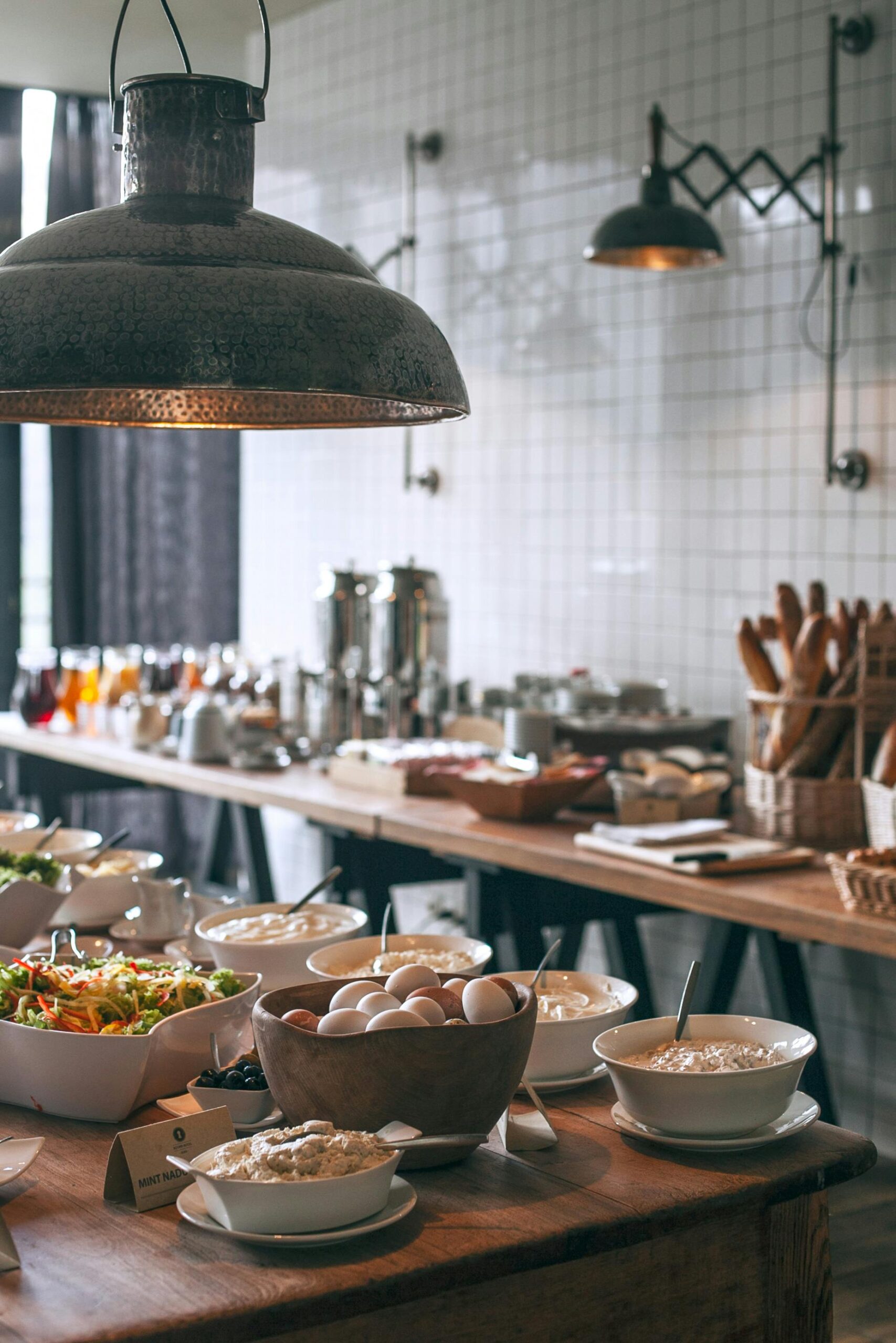 Bowls of tasty food served on banquet tables in light canteen with lamps and kitchenware and with other breakfast ingredients